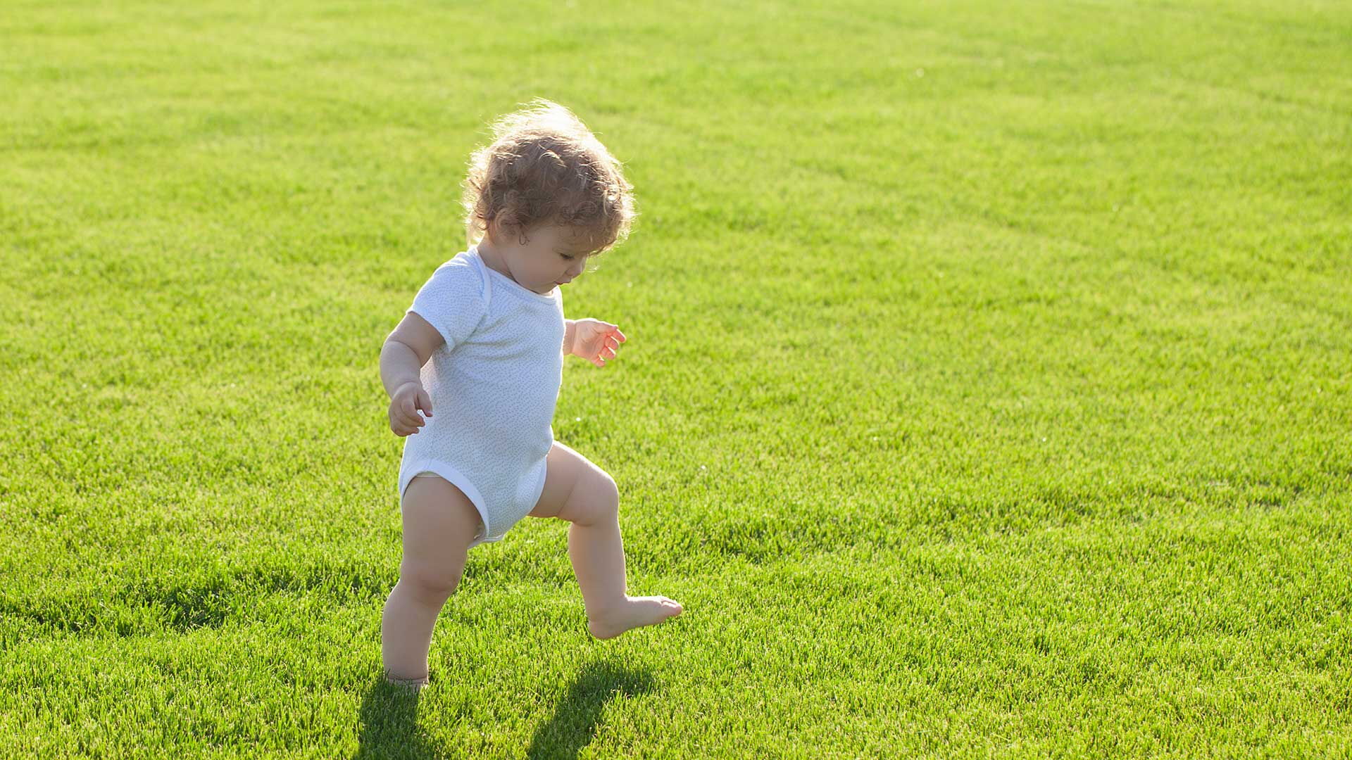 Ein Kleinkind mit Windel läuft über eine grüne Wiese