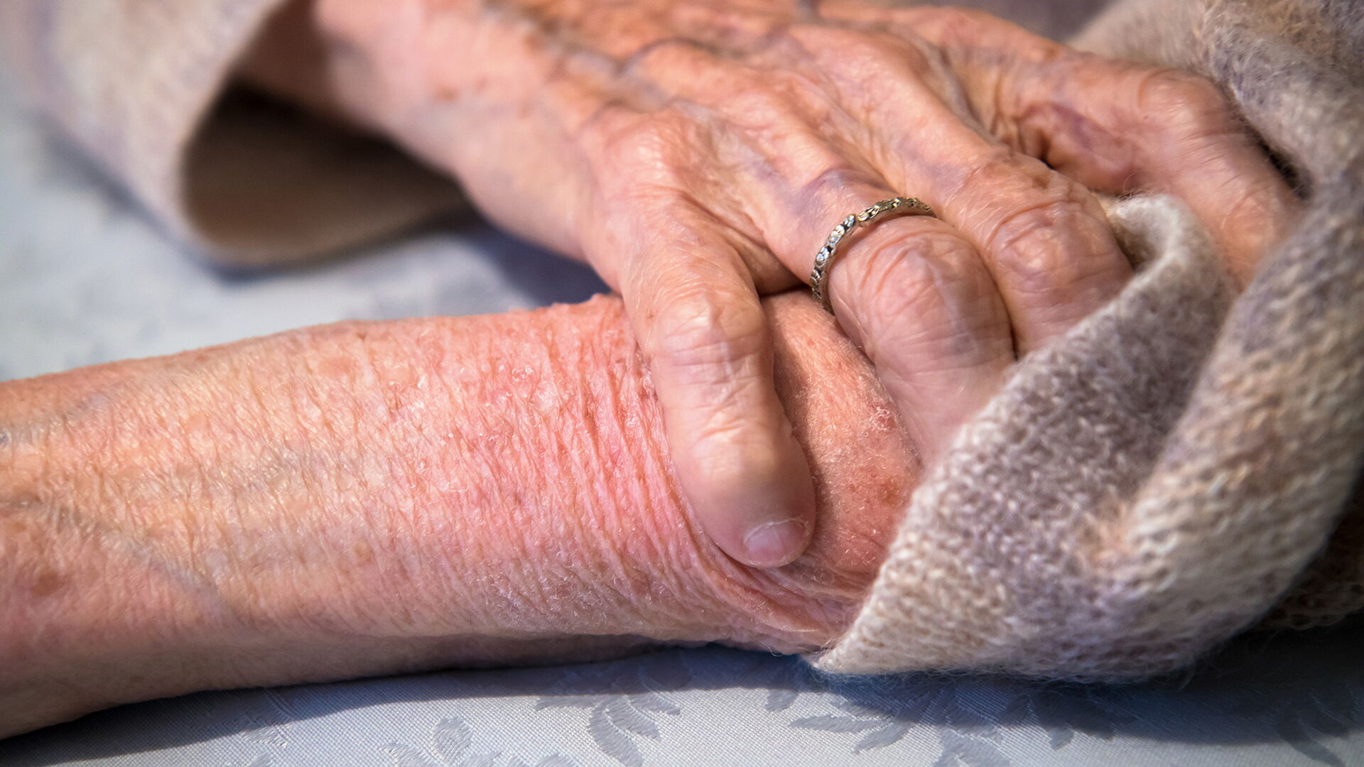 Die Hand einer älteren Person hält den anderen Arm unterhalb des Ellbogens fest. Die Haut sieht angegriffen aus.