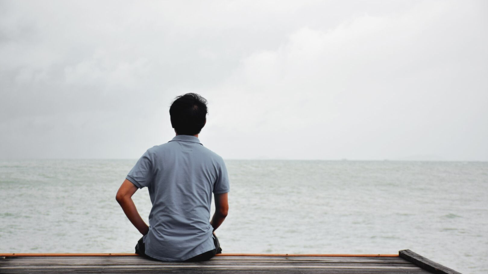 Ein Mann sitzt auf einem Steg und schaut aufs Meer