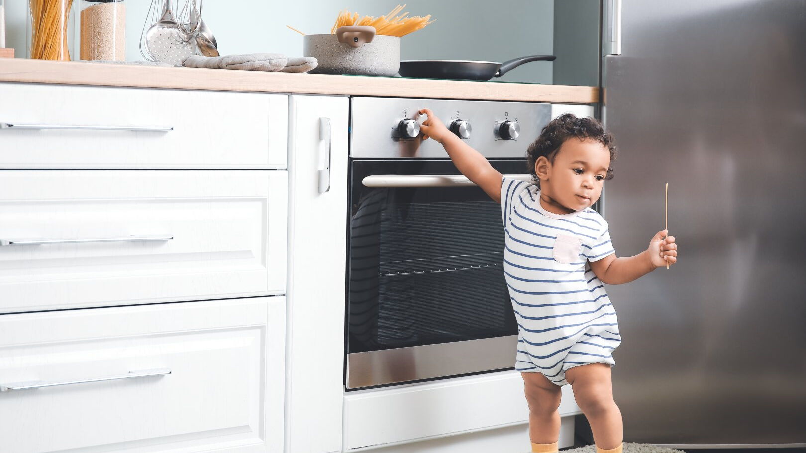 Ein Kleinkind versucht an einen heißen Topf auf einem Herd zu gelangen