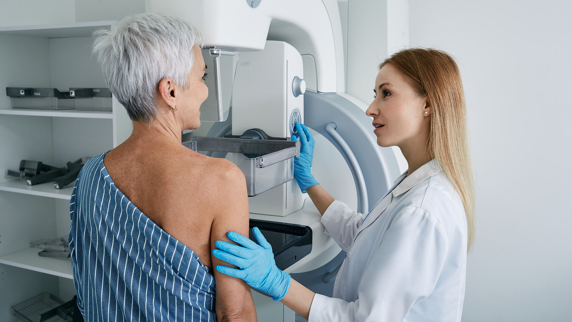Brustkrebsfrüherkennung: eine Frau steht vor einem Mammographie-Gerät, dass durch eine Ärztin bedient wird.