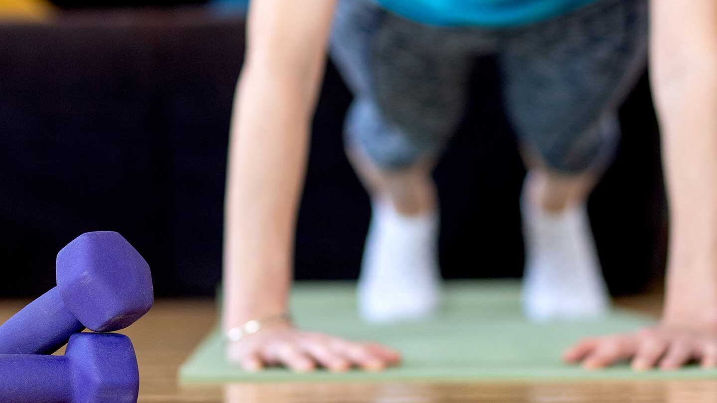 Eine Person macht Liegestütze. Links daneben liegen violettfarbene Hanteln