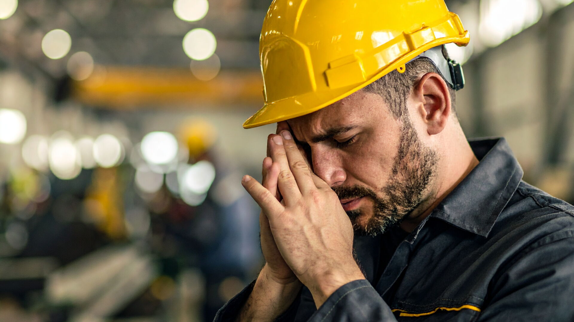 mann-in-arbeitskluft-mit-gelbem-bauhelm-sieht-verzweifelt-aus