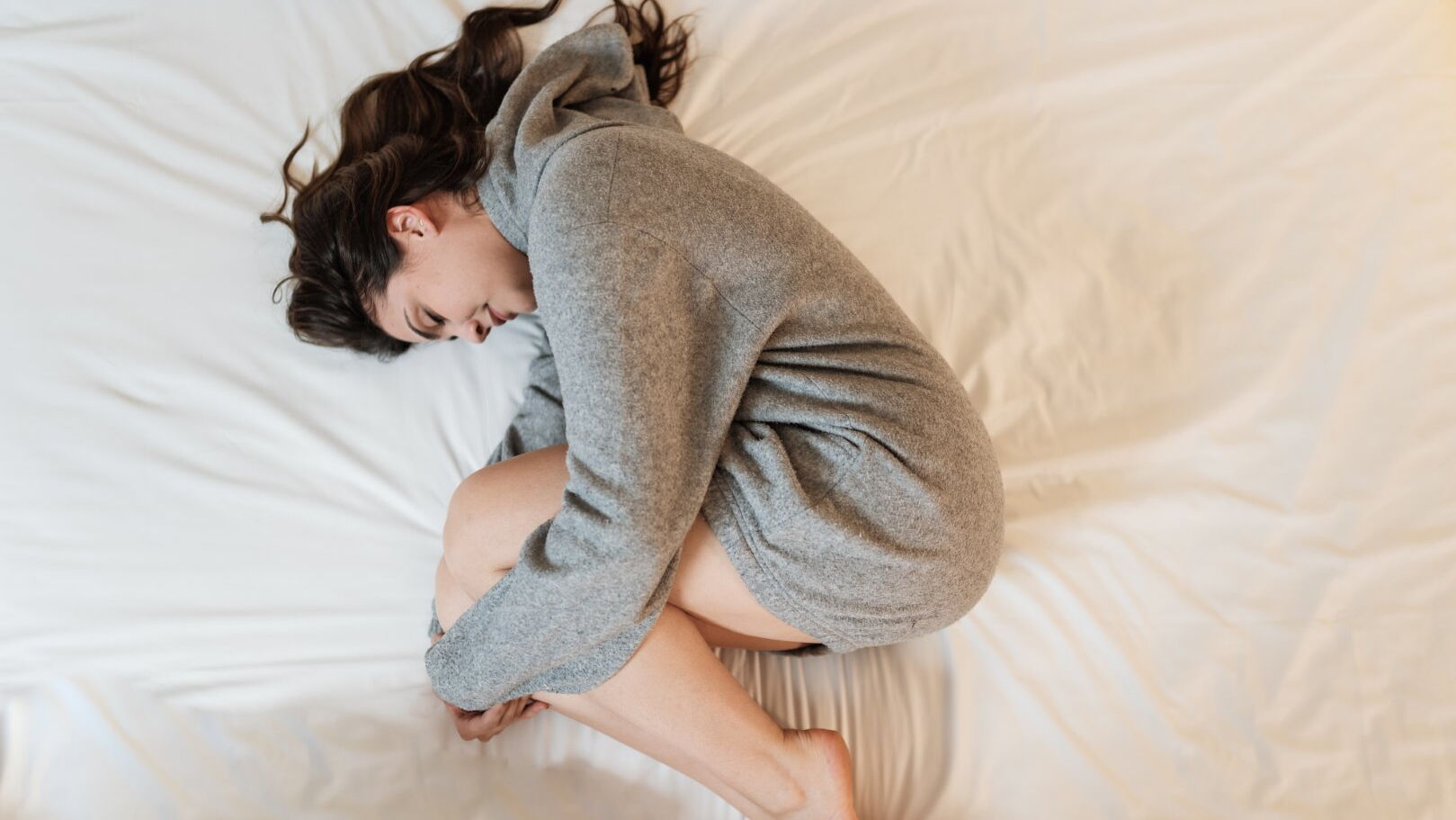 Eine Frau liegt zusammengekauert auf ihrem Bett