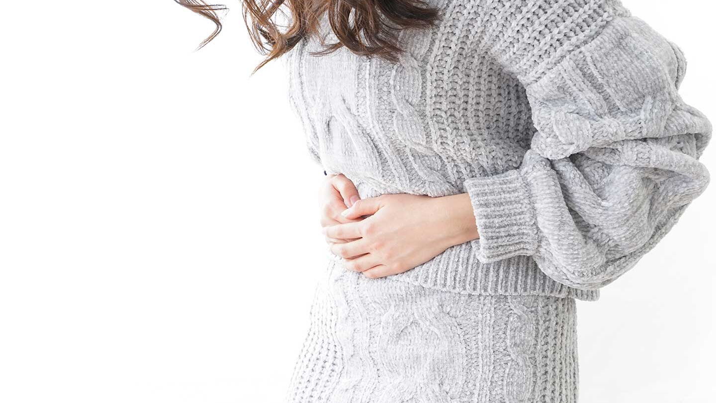 Eine junge Frau presst sich beide Hände auf den Bauch.