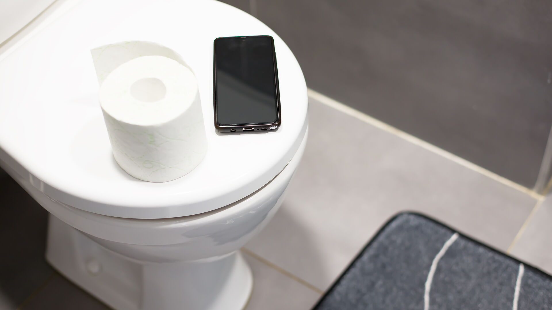 Smartphone und Toilettenpapier auf dem Toilettensitz Digitales Abhängigkeitskonzept