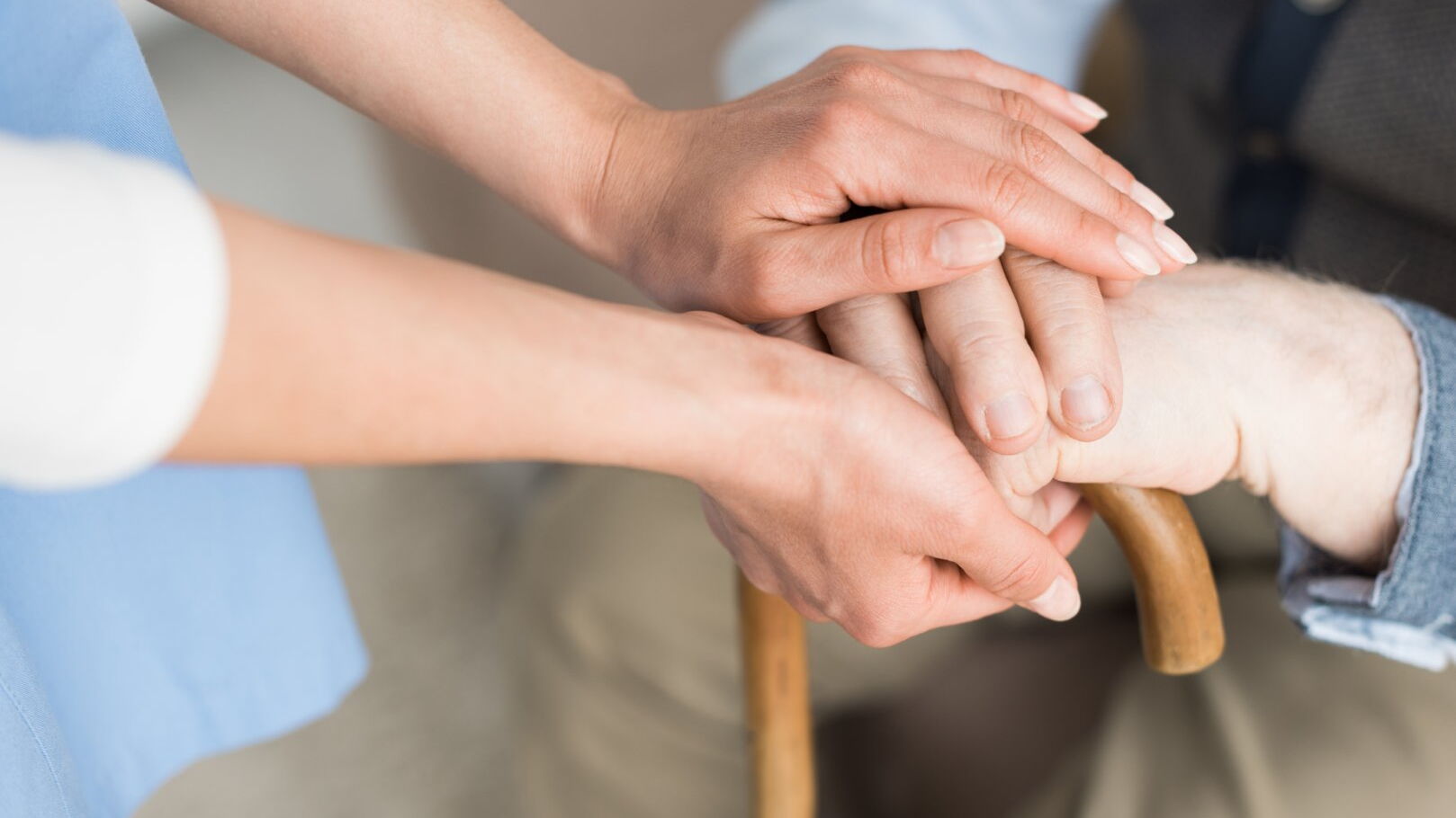 Eine Pflegekraft legt die Hände auf die Hände eines Senioren, der sich auf einem Gehstock aabstützt