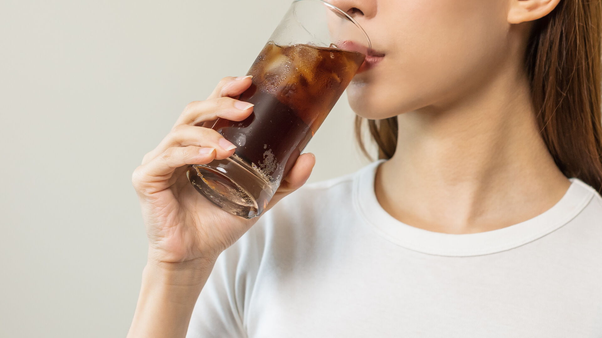 Durstige Frau trinkt oder nippt, hält ein Glas kaltes Cola mit Eis in der Hand, Erfrischung, isoliert auf weißem Hintergrund. Versuchung durch Essen.