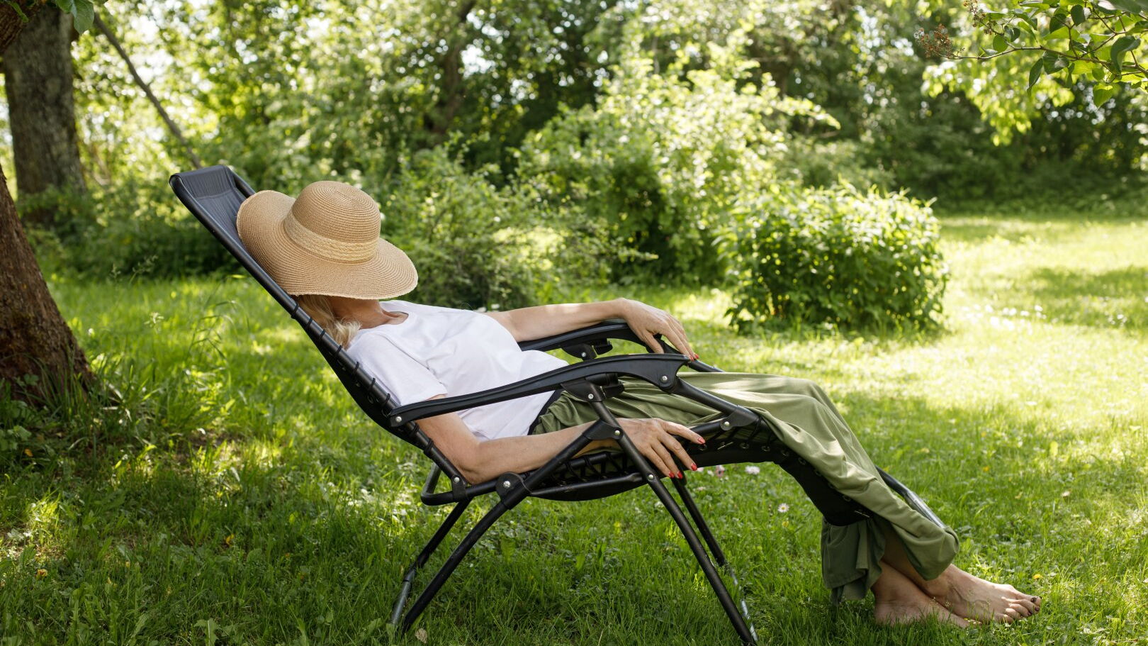 Eine Frau liegt in einem Liegestuhl im Garten und hat einen Strohhut über ihr Gesicht gelegt.