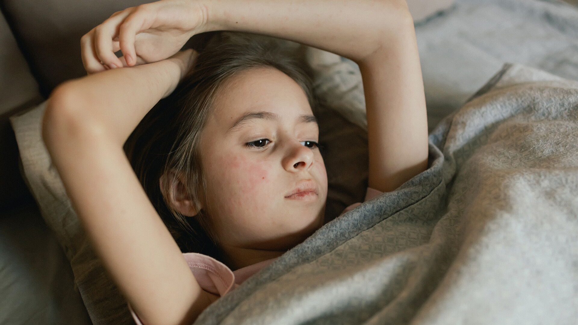 Ein Kind ruht im Bett und zeigt deutliche rote Flecken auf der Haut – möglicherweise Symptome eines Hautausschlags.
